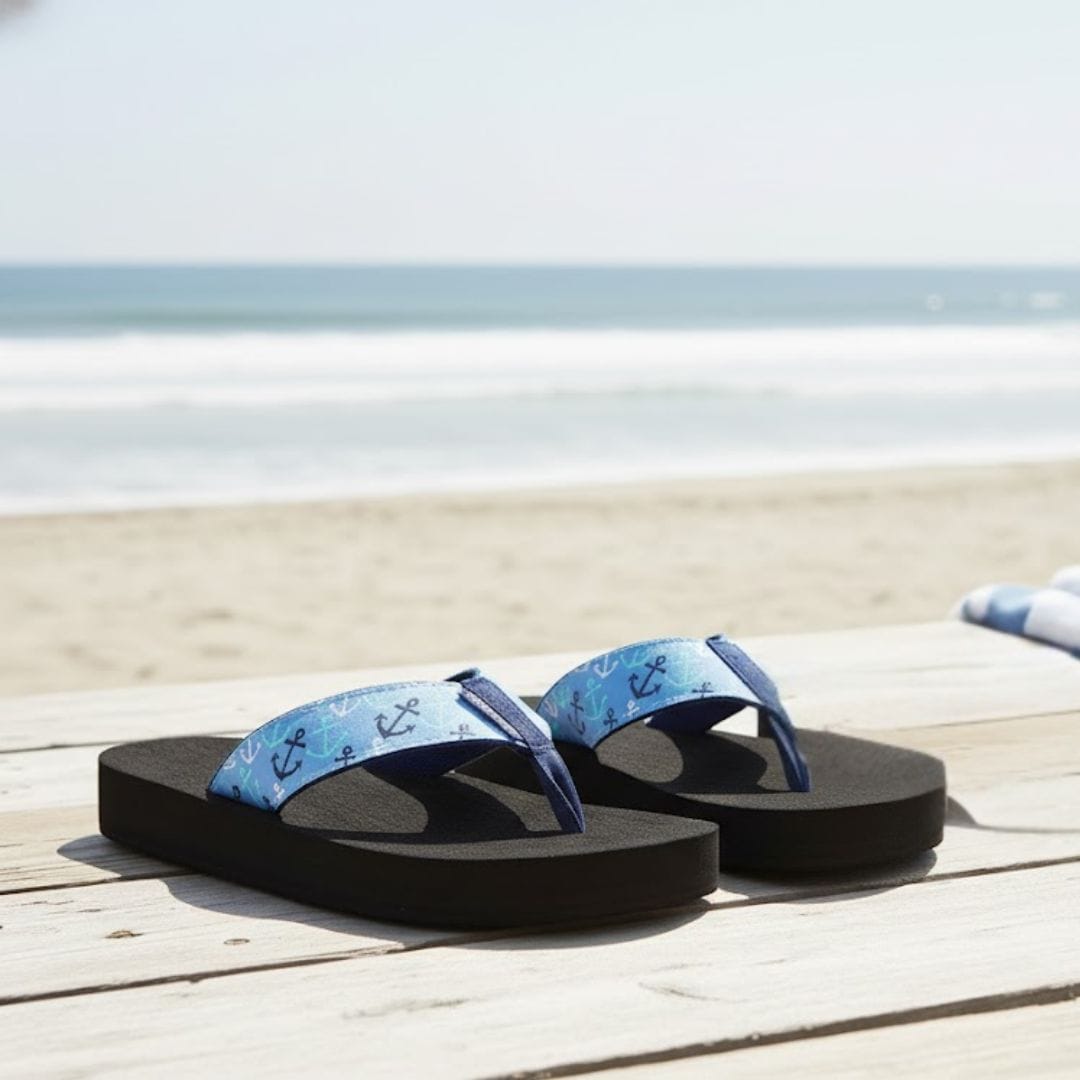 Blue flip-flops with anchor pattern on a wooden deck by the beach.