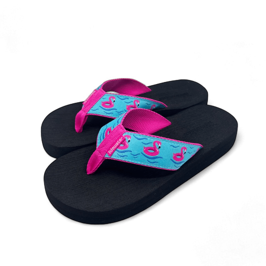 Pair of flip flops with black footbed, bright pink straps, and turquoise strap design featuring pink flamingo floats and wave details