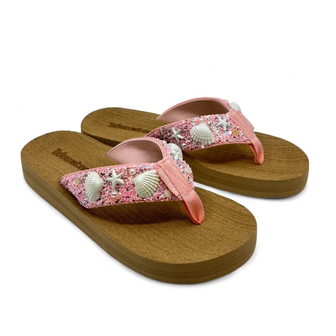 Pink flip-flops with shell and starfish embellishments on a wooden platform, perfect for beach outings.