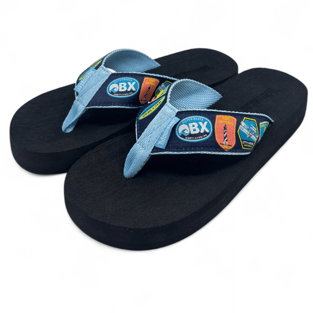 Pair of flip flops with black footbed and denim-look straps featuring OBX North Carolina beach badges and lighthouses