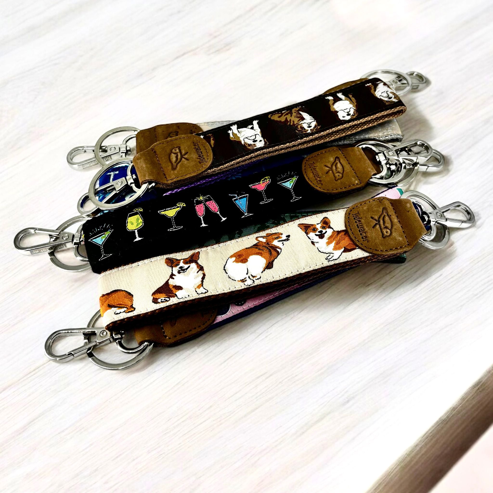 Keychain wristlets with leather accents, featuring designs of corgis, cocktails, and brown animal patterns on fabric.