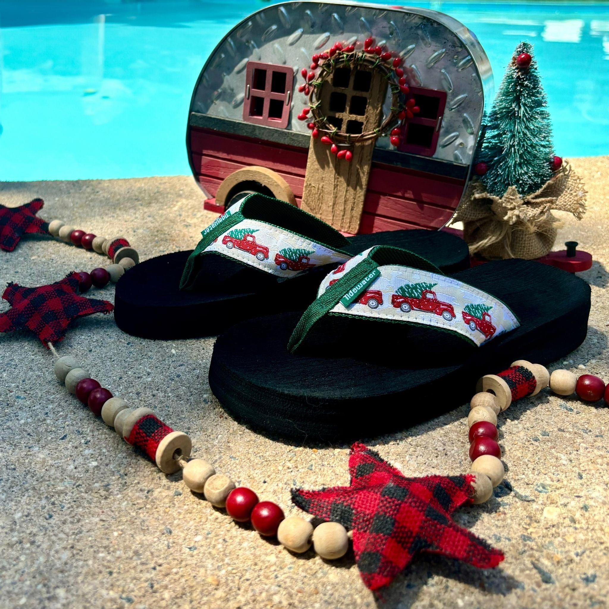Back Home Christmas sandals featuring a festive truck design, surrounded by holiday decorations by a poolside setting.
