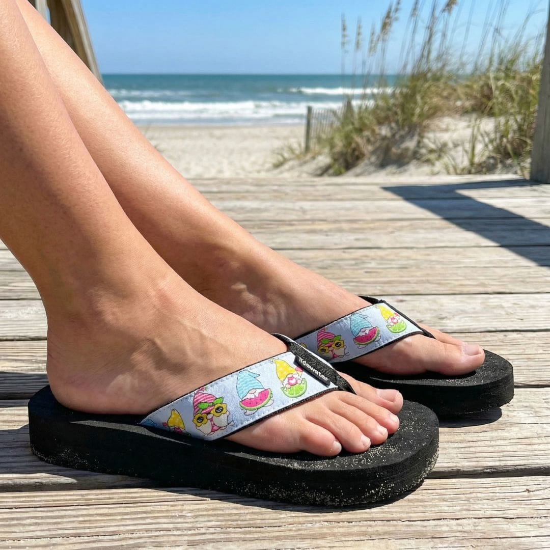 Person wearing colorful sandals on a wooden deck with a beach background