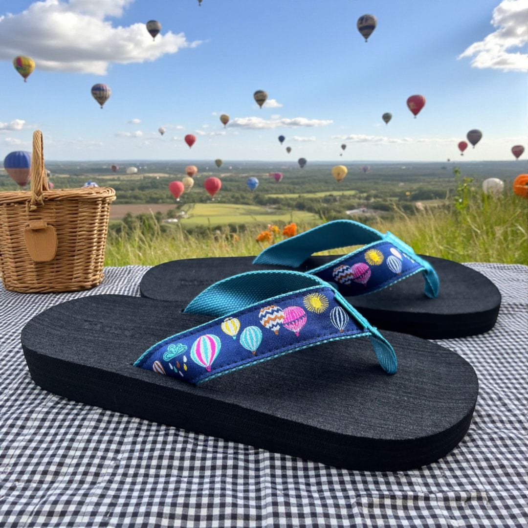 Colorful flip-flops with a hot air balloon design, set against a scenic backdrop of multiple hot air balloons in the sky.