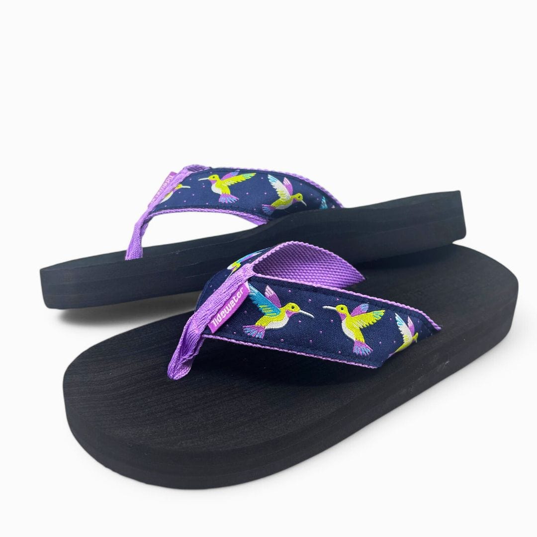 Colorful flip-flops featuring a hummingbird design on a navy background with a purple strap and black sole.