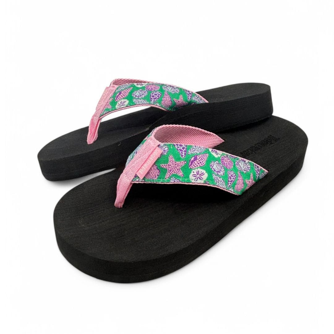 A pair of Tidewater Sandals Seashell Soiree flip flops with purple and pink seashells on a bright green strap, displayed against a white background.