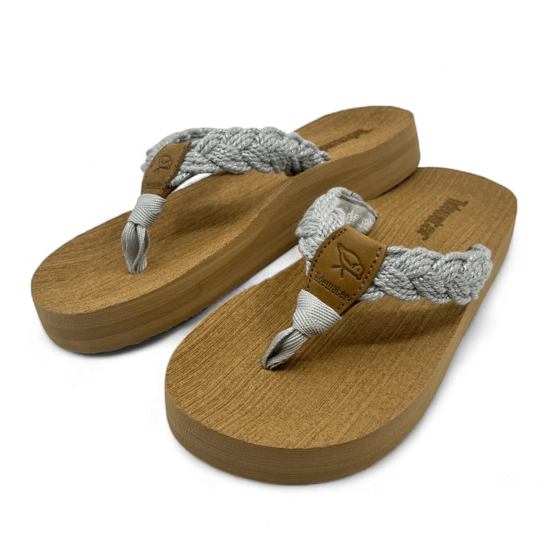 Pair of flip flops with tan comfort footbed and silver braided straps with subtle sparkle and leather accent tag

