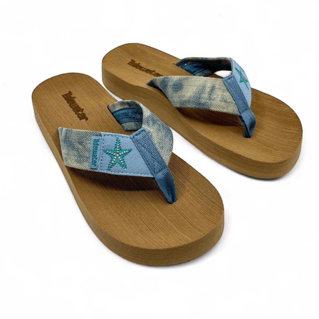 Pair of denim flip flops with teal embroidered starfish on light blue straps and brown comfort footbed

