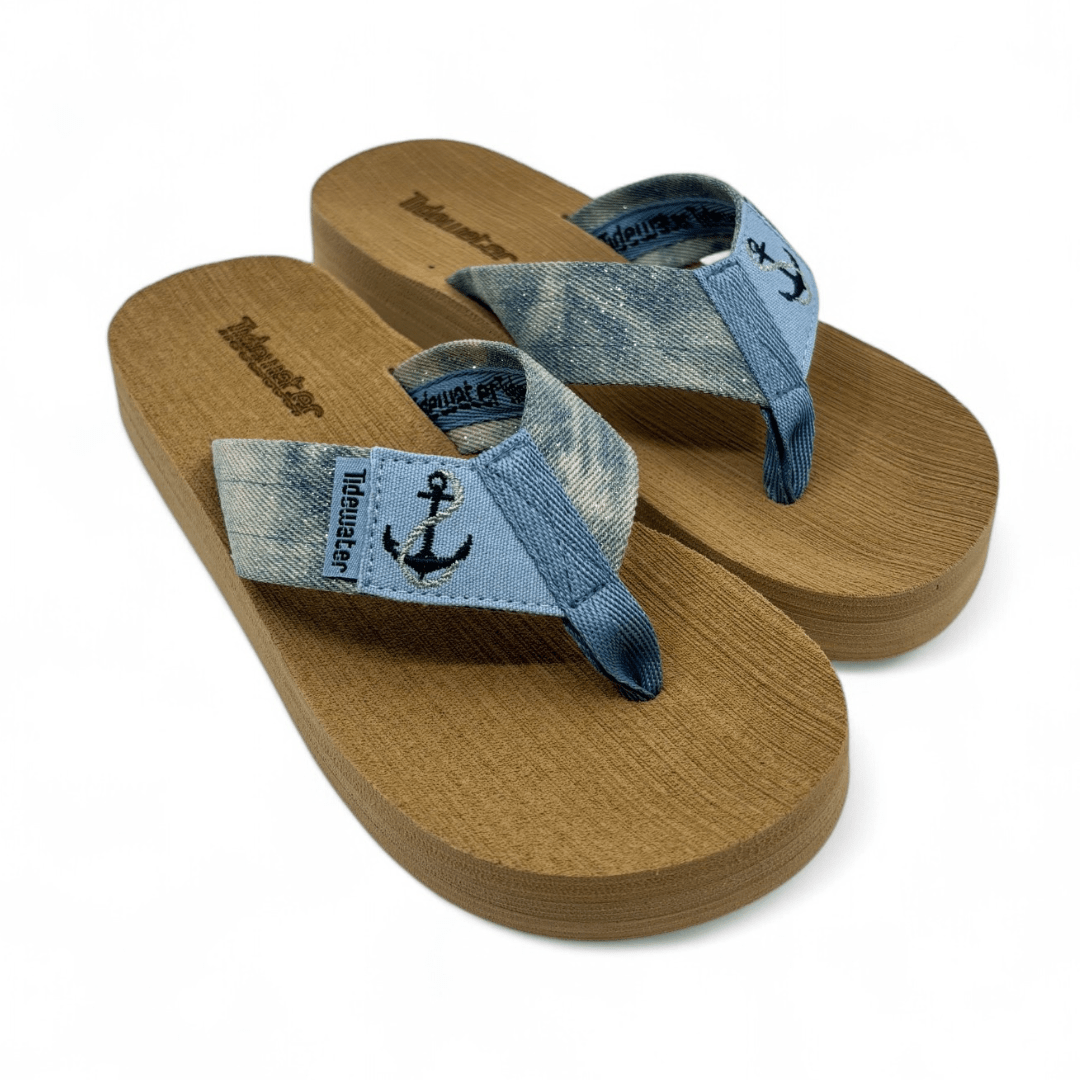 Brown flip-flops with faded denim straps, anchor embroidery, and “Tidewater” branding, shown on beach and white backgrounds